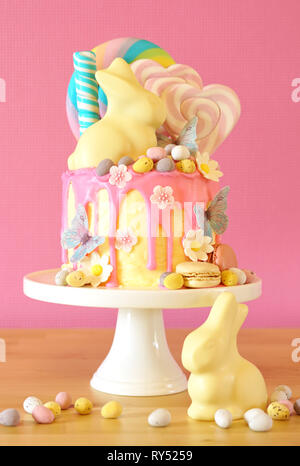 On-trend Easter theme candy land drip cake decorated with lollipops, candy eggs and white chocolate bunny in party table setting. Stock Photo