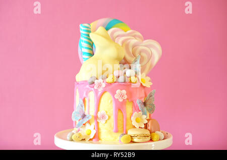 On-trend Easter theme candy land drip cake decorated with lollipops, candy eggs and white chocolate bunny in party table setting. Stock Photo