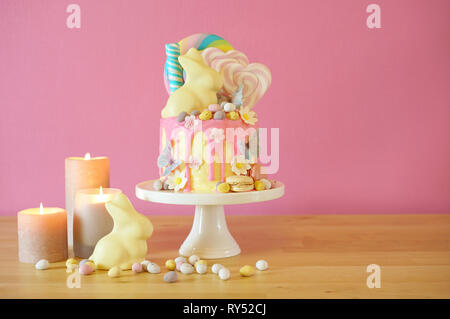 On-trend Easter theme candy land drip cake decorated with lollipops, candy eggs and white chocolate bunny in party table setting. Stock Photo