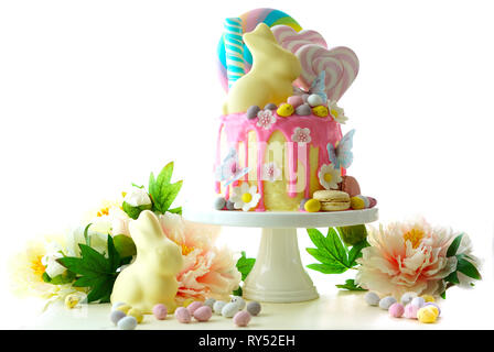 On-trend Easter theme candy land drip cake decorated with lollipops, candy eggs and white chocolate bunny in party table setting. Stock Photo