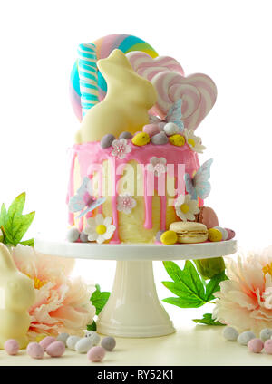 On-trend Easter theme candy land drip cake decorated with lollipops, candy eggs and white chocolate bunny in party table setting. Stock Photo