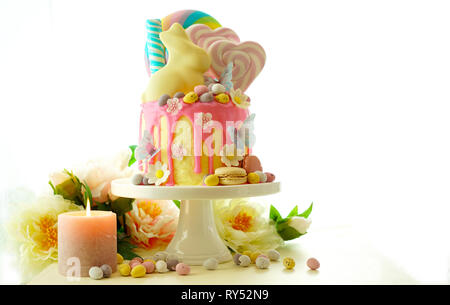 On-trend Easter theme candy land drip cake decorated with lollipops, candy eggs and white chocolate bunny in party table setting. Stock Photo