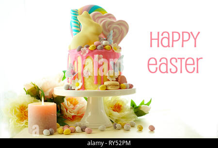 On-trend Easter theme candy land drip cake decorated with lollipops, candy eggs and white chocolate bunny in party table setting. Stock Photo