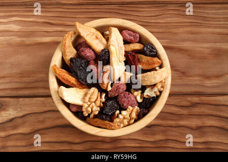 Mix of dried fruit pieces of apple and pear, dried blue plums, strawberries, raspberries, cherries and walnuts in a bamboo bowl on a wooden table. Stock Photo