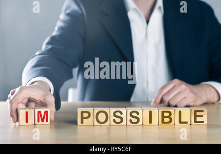 Business man puts away first two letters from the word impossible, so it becomes possible; management or solution finding concept, blue toned with lig Stock Photo