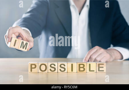 Business man puts away first two letters from the word impossible, so it becomes possible; management or solution finding concept, blue toned with lig Stock Photo