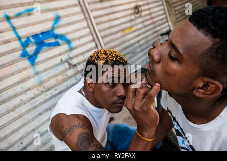 A young Colombian man shaves a friend’s beard with a razor blade in the market of Bazurto, Cartgena, Colombia. Stock Photo