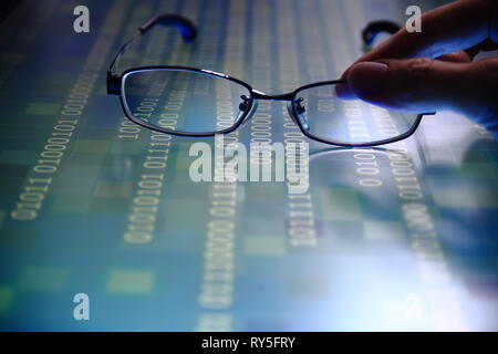 hand reaching for glasses on digital led displaying multiple layers of binary code computer data matrix. big data analytics and digital language conce Stock Photo