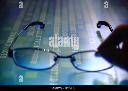 hand reaching for glasses on digital led displaying multiple layers of binary code computer data matrix. big data analytics and digital language conce Stock Photo
