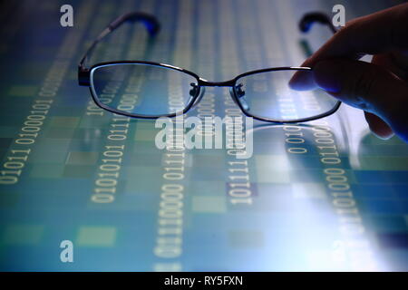 hand reaching for glasses on digital led displaying multiple layers of binary code computer data matrix. big data analytics and digital language conce Stock Photo