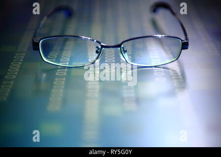 big data analysis. glasses placed on a LED digital panel display white light one and zero binary text number in moving motion pattern. modern technolo Stock Photo