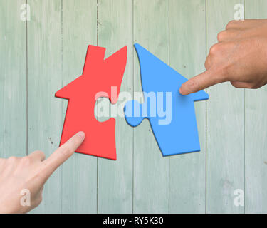 Woman and man two hands assembling house shape puzzles of different color red and blue, high angle view, on wooden plank background. Stock Photo
