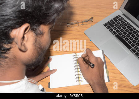 Businessman writing in his diary. Open notebook with blank pages next to cup of coffee and eyeglasses on wooden table. Business still life concept wit Stock Photo