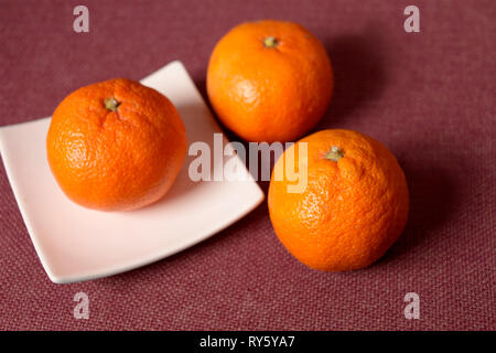 Three oranges n a plate placed on red textile, studio closeup Stock Photo