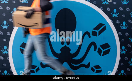 12 March 2019, Lower Saxony, Garbsen: An employee of the parcel shipper Amazon can be seen in the sorting centre in Garbsen in front of a picture showing an octopus distributing a parcel. Amazon sorts the parcels in Garbsen by delivery area and then forwards them to parcel delivery agents. Amazon already operates a logistics centre in Winsen in Lower Saxony. 700 jobs are to be created in Garbsen near Hanover. Photo: Peter Steffen/dpa Stock Photo