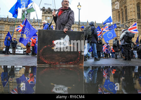 Westminster, London, UK. 12th Mar, 2019. Artist and Painter Kaya Mar with one of his satirical paintings commenting on Brexit. Pro Brexit and Anti Brexit supporters protest outside the Houses of Parliament in Westminster on the day that has a 'meaningful vote' in Parliament on Theresa May's Brexit Deal scheduled for the evening. Credit: Imageplotter/Alamy Live News Stock Photo