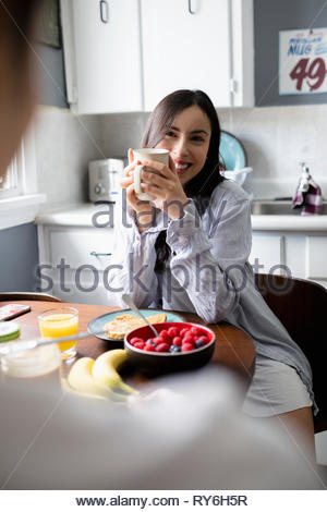 Happy young Latinx woman enjoying breakfast with boyfriend in kitchen