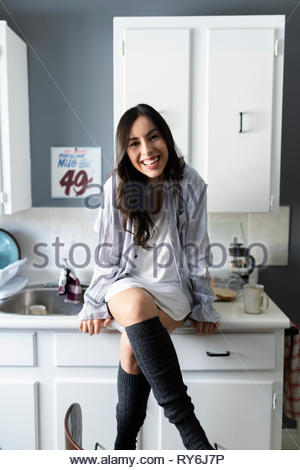 Portrait happy young Latinx woman sitting on kitchen counter