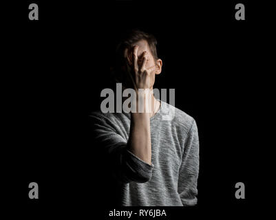 Man covering face with hand while standing against black background Stock Photo