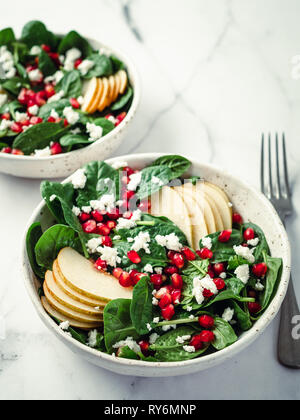 Fresh salad with baby spinach, pear, pomegranate and cottage cheese. Two bowls with delicious summer fruit salad on marble table. Copy space for text. Ideas and recipes for healthy breakfast or lunch Stock Photo