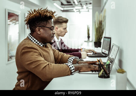 Concentrated busy guys working with their laptops while sitting together Stock Photo