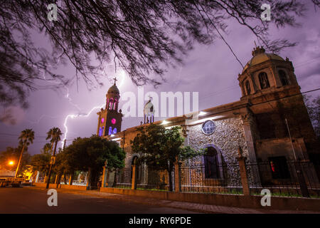 Lightning strikes behind a historic mission church on a plaza in the colonial Mexican town of Baviacora, in Sonora, Mexico during the Summer Monsoon. Stock Photo