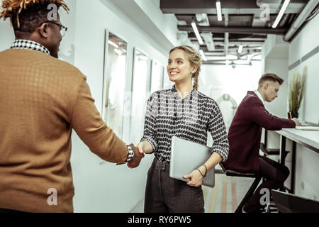 Cheerful young lady in black and white shirt greeting new workmate Stock Photo