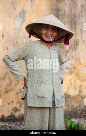 Smiling Old Vietnamese Woman Smoking Cigarette With Hands on Hips  -  Hoi An, Vietnam Stock Photo