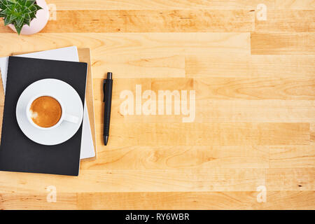 Cup of coffee or espresso on bunch of notebooks with pen and plant on yellow wooden table. Top view. Copy space for text. Flat lay. Stock Photo