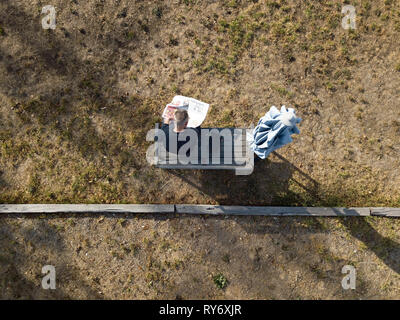 Australian pensioner or old man reading newspaper outside, sitting on outdoor bench in a grassed area. Aerial photography in Victoria, Australia. Stock Photo