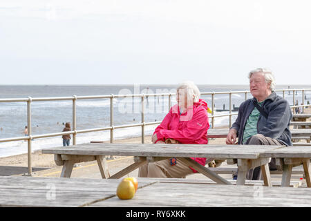Southwold, UK - September 10, 18 - Senior couple sitting on the seaside table bench looking over the Southwold beach Stock Photo