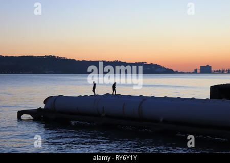 silhouette from two boys running on pipes in a pier at the sunset. Stock Photo