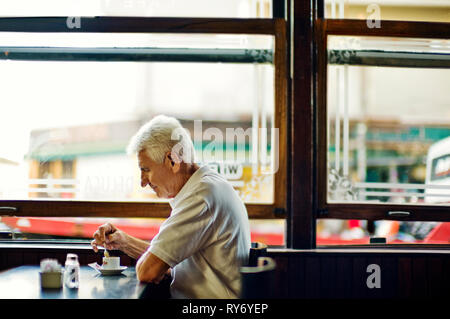 Mature man sitting alone at restaurant table with cup of coffee. Stock Photo