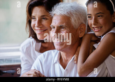 Girl sitting happily with her grandparents, leaning on her grandfather's shoulder. Stock Photo