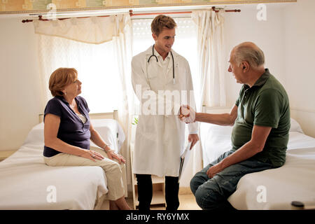 Young doctor greeting female patient and her husband in hospital room. Stock Photo