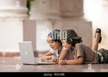Brother and sister looking at a laptop on a tiled patio. Stock Photo