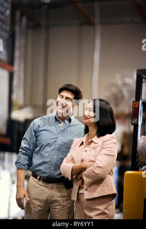 Two smiling colleagues discussing work in a warehouse. Stock Photo