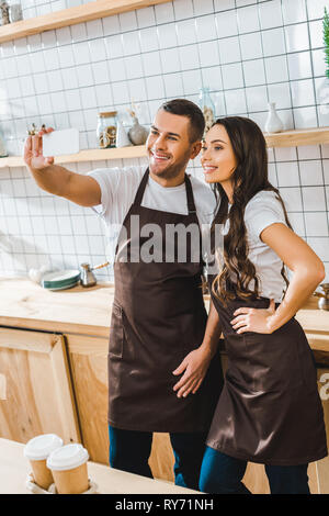 cashiers in aprons standing and taking selfie in coffee house Stock Photo