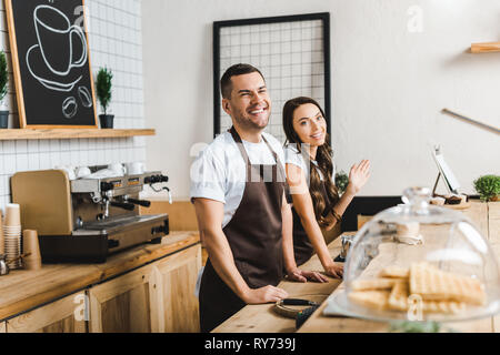 cashiers in aprons standing and smiling behind bar counter in coffee house Stock Photo