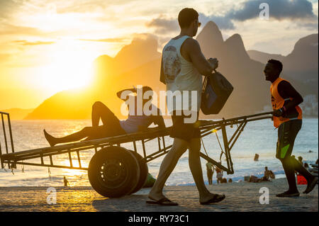 RIO DE JANEIRO - MARCH 20, 2017: Young Brazilian workers push an empty cart at Arpoador, where locals and tourists gather to watch Ipanema sunset. Stock Photo