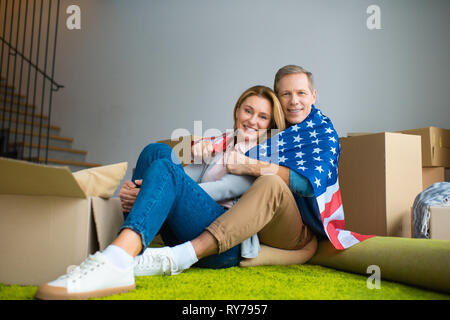 happy couple wrapping in usa national flag and looking at camera Stock Photo