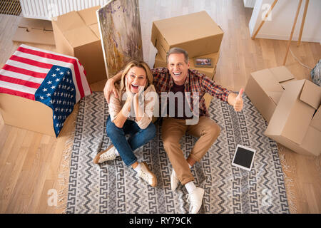 happy excited couple sitting on fleece blanket on floor at new home and looking at camera Stock Photo