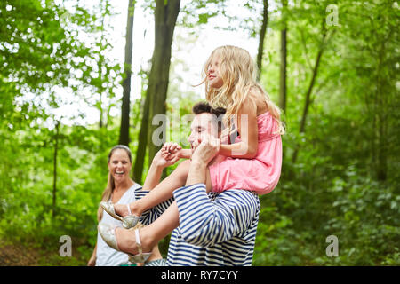 Family is taking a trip in the forest with daughter piggybacking with father Stock Photo
