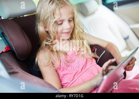 Little girl in the car with tablet. Computer makes a computer game Stock Photo