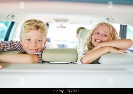 Two children in the back seat in the car are looking forward to the summer holidays Stock Photo