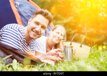 Happy couple having coffee in tent while camping in summer Stock Photo