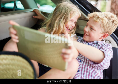 Sibling couple is having fun in the car while playing with the tablet computer Stock Photo