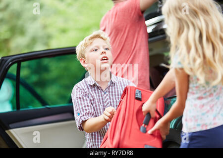 Siblings at the car helping together while packing their bags before traveling Stock Photo