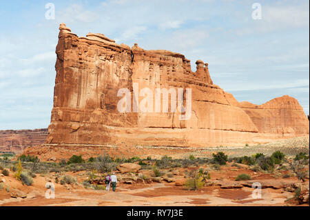 Two hikers approaching a gigantic sandstone formation known as the Tower of Babel on Park Avenue trail in Arches National Park, Utah, USA. Stock Photo