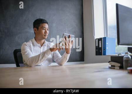 Smiling Asian businessman working on his tablet in an office Stock Photo